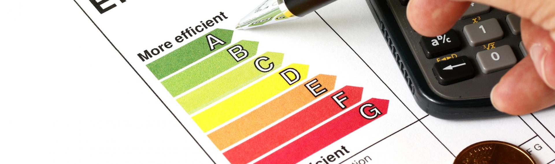 Hand Pointing A Pen Toward an Energy Index Next To A Calculator