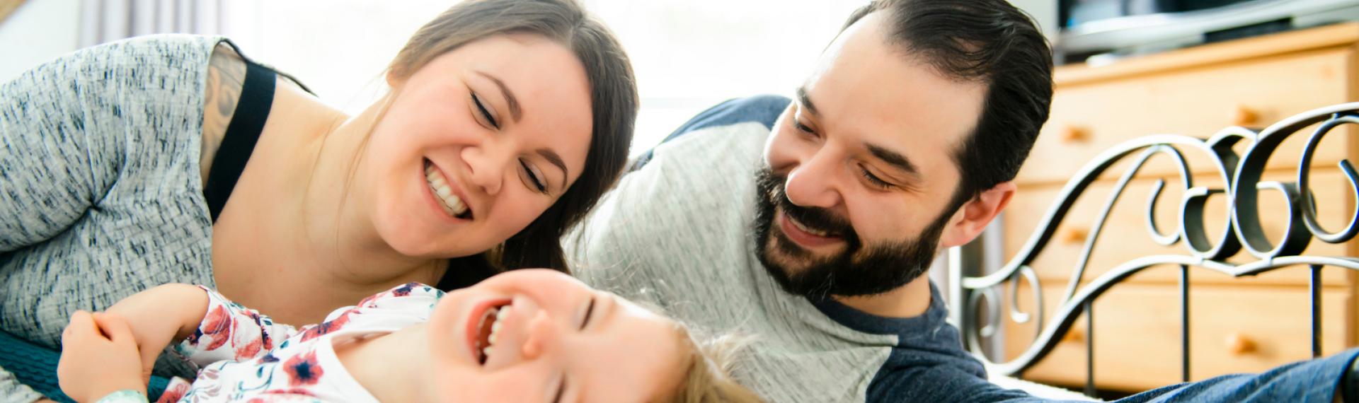 Parents Playing And Laughing With Child On Bed